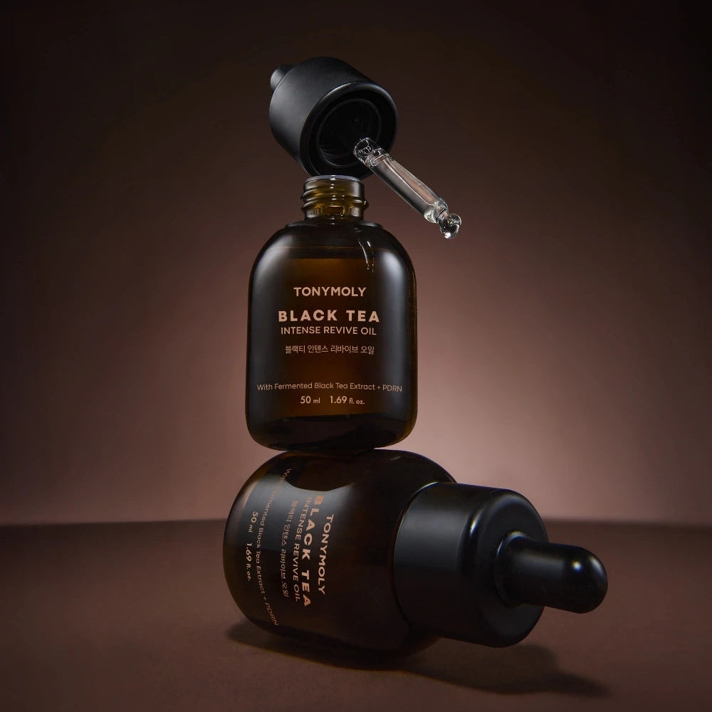 Décris l'image en français : TONY MOLY Black Tea Intense Revive Oil 50ml, flacon et reflet, ambiance sombre.