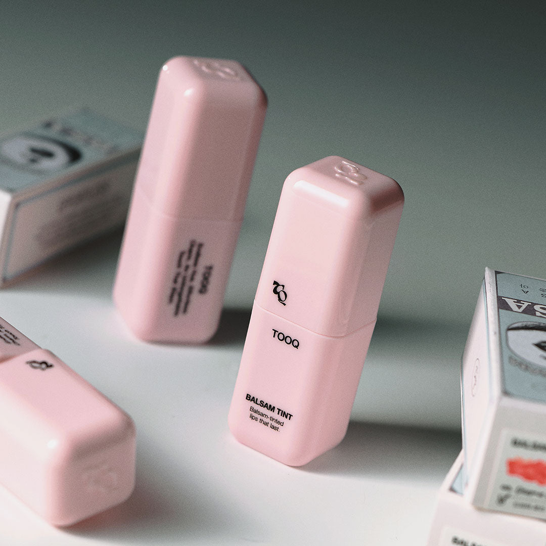 TOOQ Balsam Tint de la marque TOOQ, pack rose sur fond vert avec boîtes cosmétiques, photo produit en studio