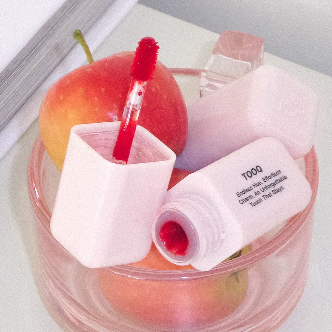 TOOQ Balsam Tint de TOOQ, flacon rose appliqué sur pastèque rouge, dans un décor produit cosmétique.