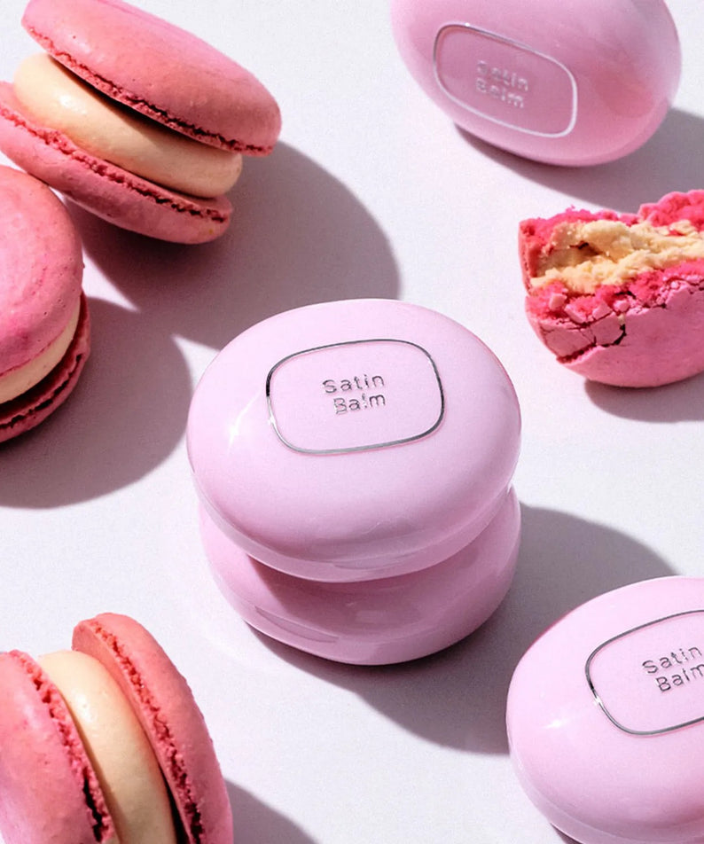 TOOQ Satin Peach Blossom avec macarons roses en fond, produit de beauté élégant et moderne mis en valeur sur une surface blanche.