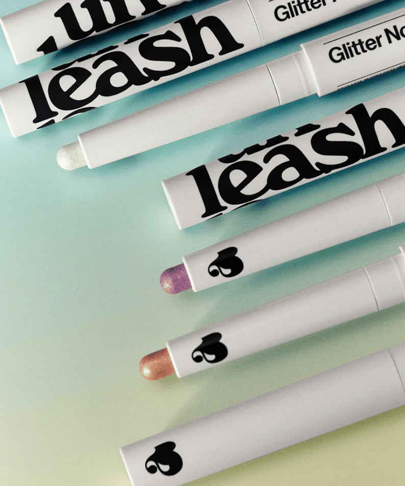 Lignes de UNLEASHIA Pretty Easy Glitter Stick sur fond pastel, parfait pour des maquillages scintillants et glamour.