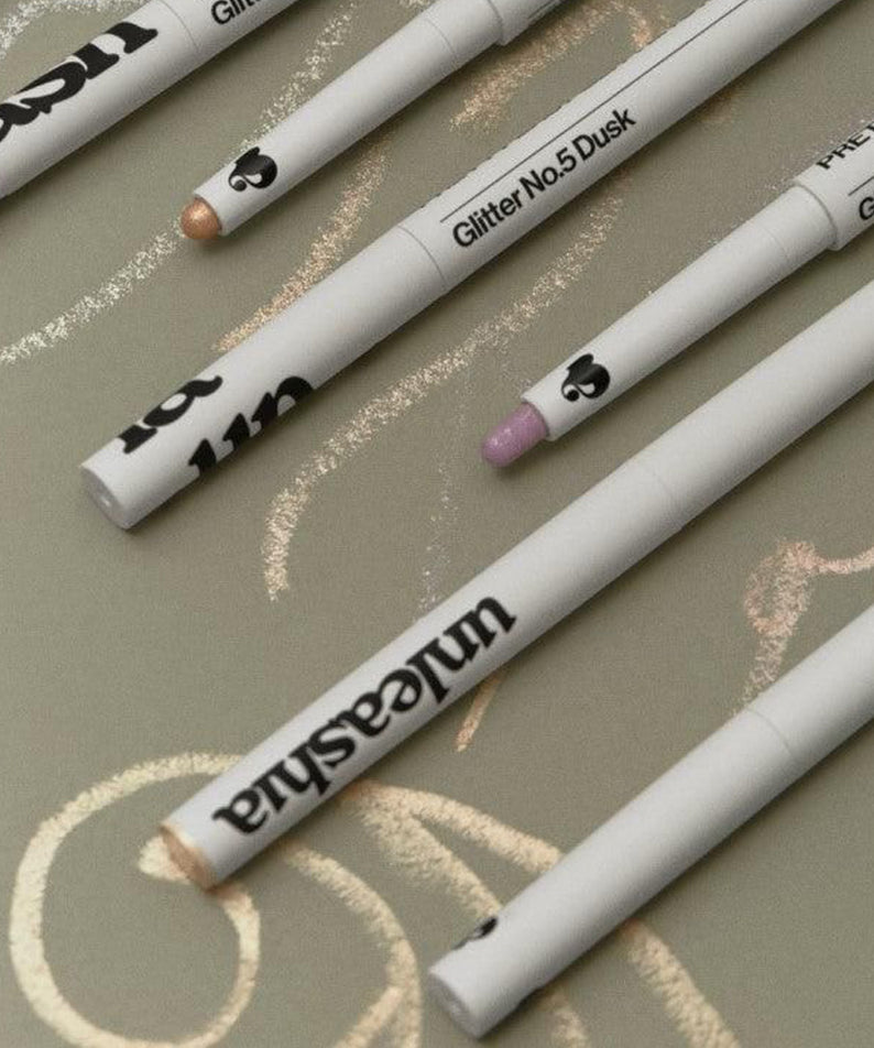 UNLEASHIA Pretty Easy Glitter Stick en plusieurs nuances sur fond créatif.