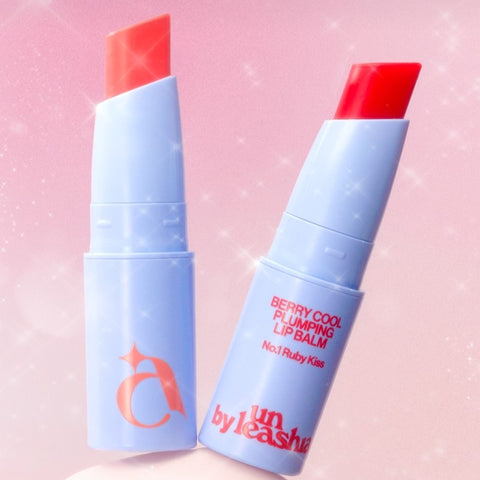 UNLEASHIA the Berry Cool Plumping Lip Balm, tube lèvres rose et bleu sur fond rose, style cosmétique.