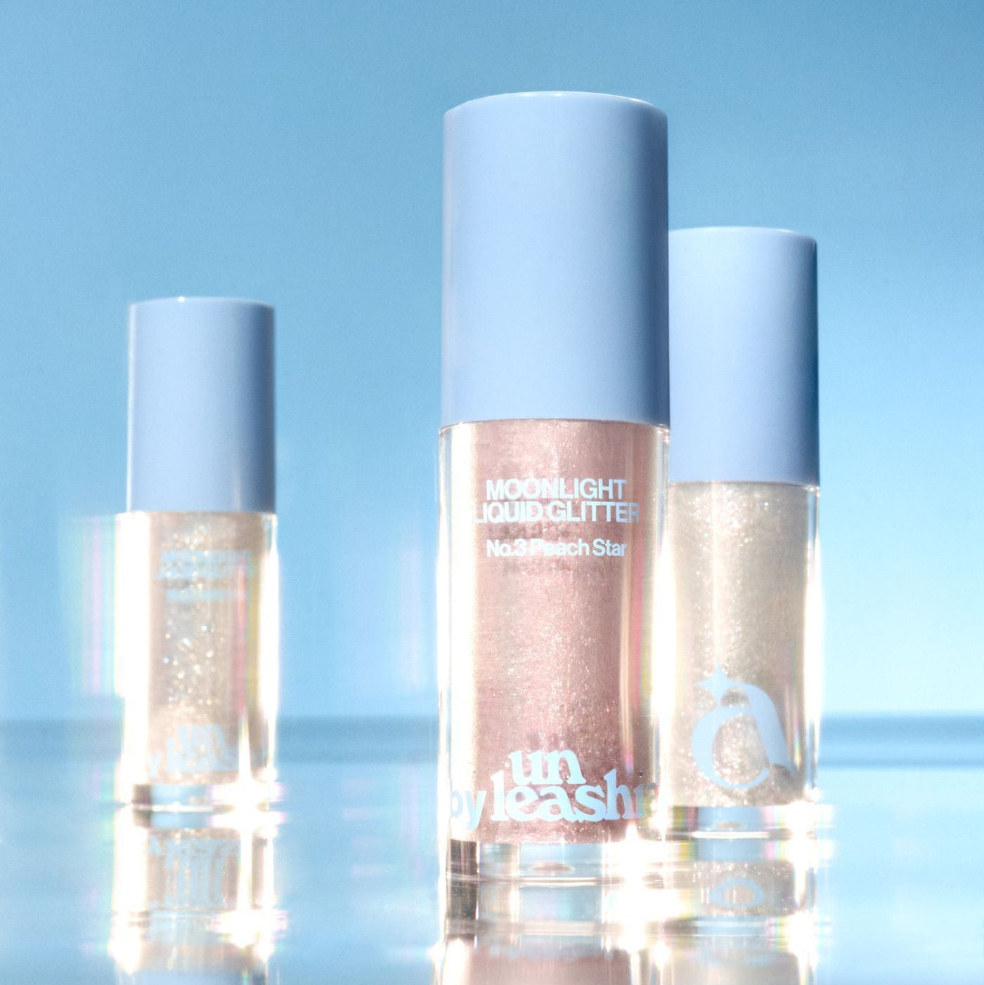 UNLEASHIA the Moonlight Liquid Glitter, flacons nacrés sur fond bleu ciel, éclat liquide scintillant de la marque UNLEASHIA.