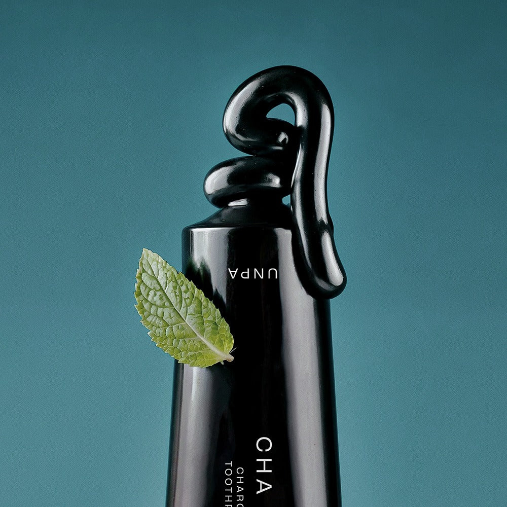 UNPA Cha Cha Charcoal Original Toothpaste 100g de la marque UNPA, tube noir sur fond bleu, feuilles de menthe à côté
