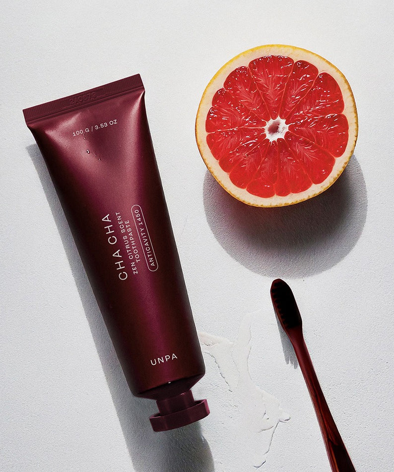 UNPA Cha Cha Zen Grapfruit Scent 1450 High Fluoride Toothpaste 100g UNPA sur fond blanc avec tranche de pamplemousse et brosse.