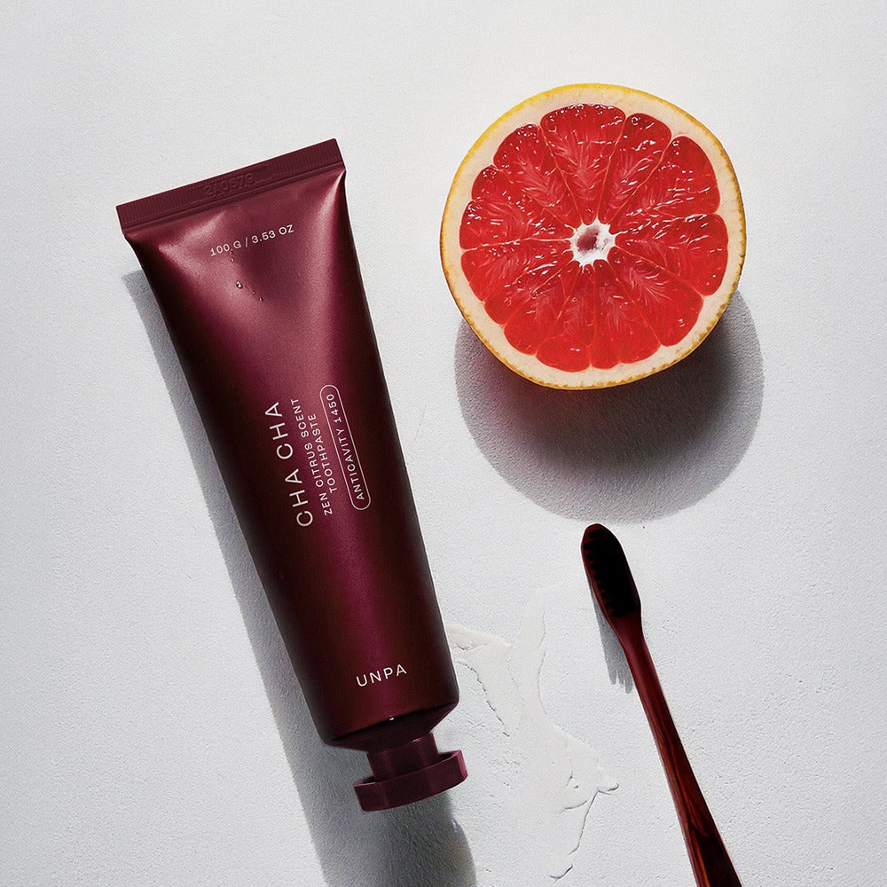 UNPA Cha Cha Zen Grapfruit Scent 1450 High Fluoride Toothpaste 100g UNPA sur fond blanc avec tranche de pamplemousse et brosse.