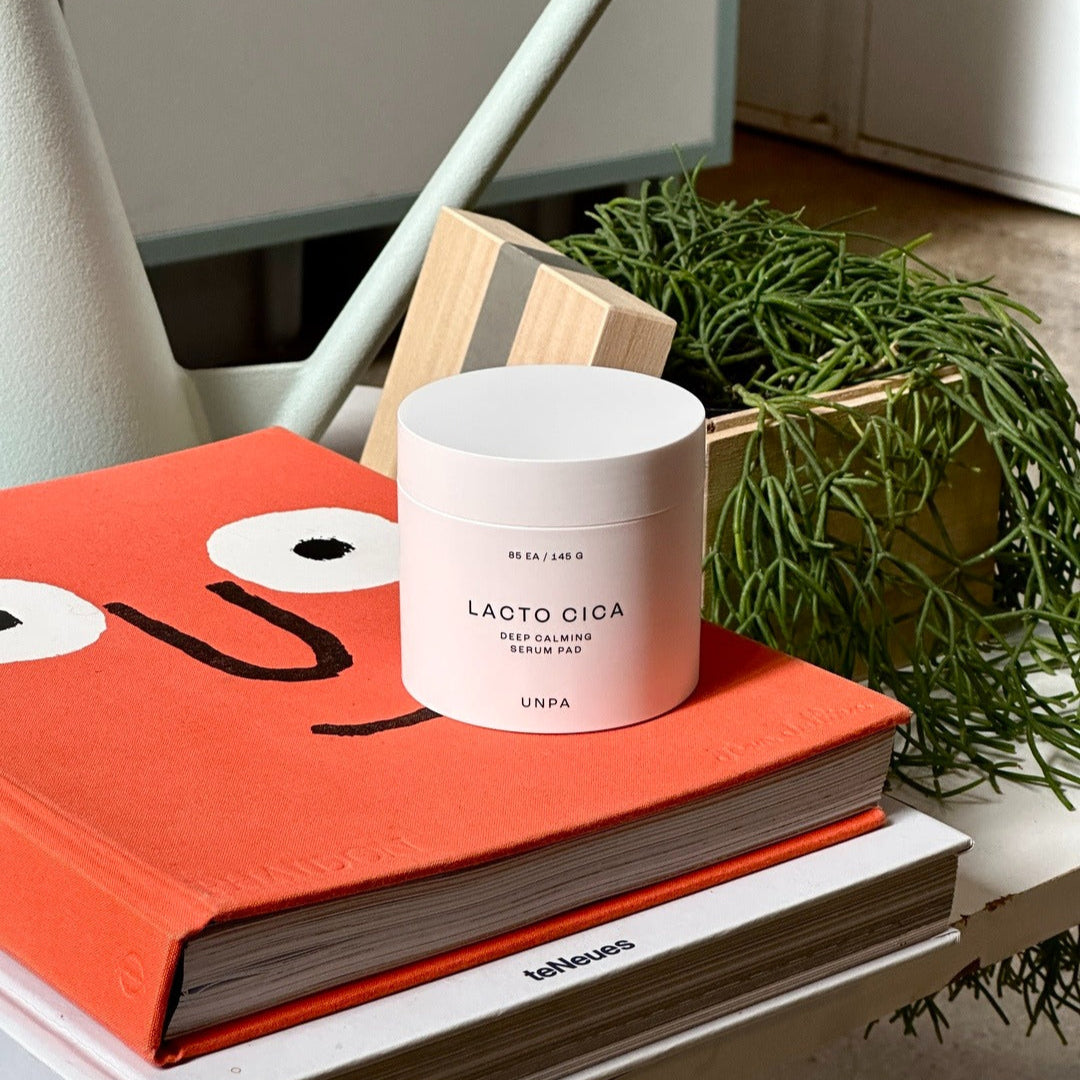 UNPA Lacto Cica Deep Calming Serum Pad 85 Sheets UNPA, pot sur livres et plante verte, ambiance salle de soins