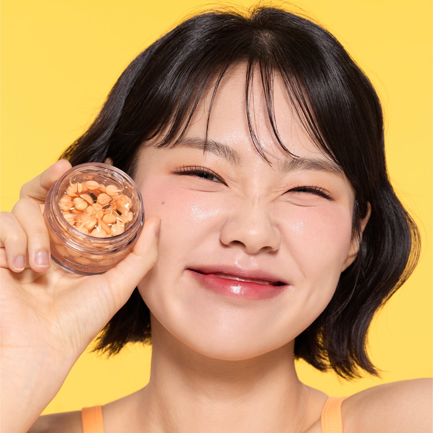 VT COSMETIC Vitamin C Astaxanthin Capsule Cream 50ml, photo beauté sur fond jaune, femme tenant un pot de capsules décoratives.