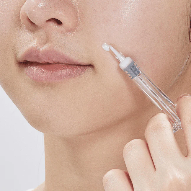 VT COSMETICS Riddle Shot 1300 8ml, sérum en goutte, appliqué au compte-gouttes sur le visage, fond clair, gros plan.