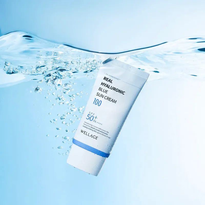 WELLAGE  Real Hyaluronic Blue Sunscreen 50ml : tube bleu sur peau, gouttelettes d’eau, visuel rafraîchissant.
