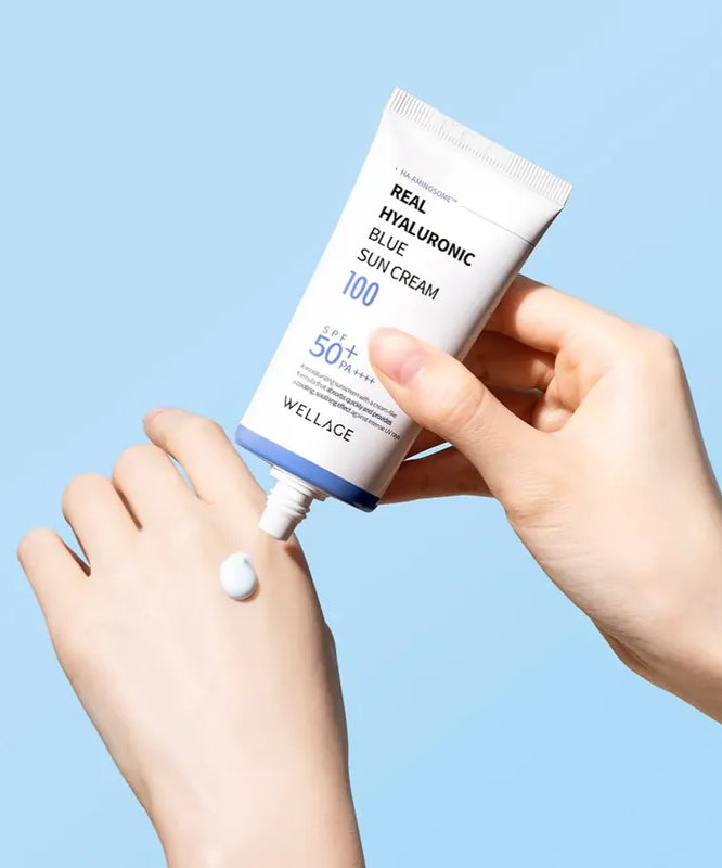 WELLAGE  Real Hyaluronic Blue Sunscreen 50ml : tube crème solaire, main l’ouvrant, contexte bleu, texte lisible.