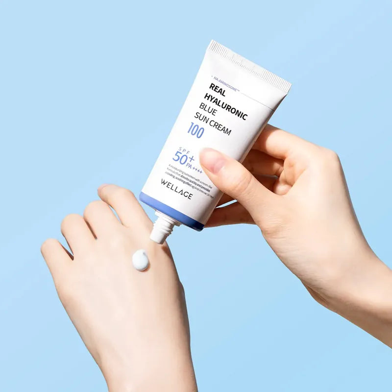WELLAGE  Real Hyaluronic Blue Sunscreen 50ml : tube crème solaire, main l’ouvrant, contexte bleu, texte lisible.