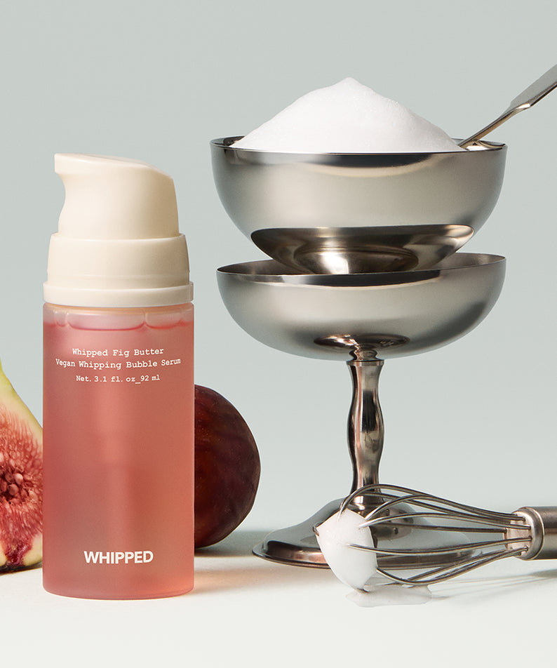 WHIPPED Butter Vegan Whipping Bubble Serum 92ml, flacon rose, fouet en arrière-plan, ambiance soin cosmétique végane.