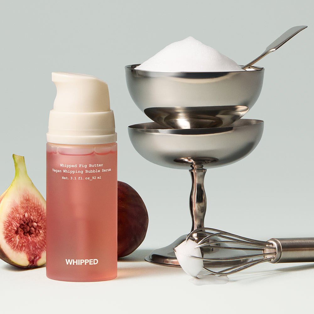 WHIPPED Butter Vegan Whipping Bubble Serum 92ml, flacon rose, fouet en arrière-plan, ambiance soin cosmétique végane.
