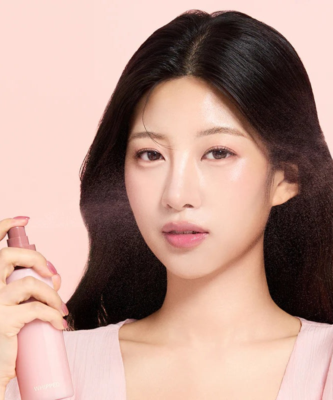 Femme tenant le WHIPPED Butter Vegan Milk Foam Pack Mist 150ml, brume hydratante pour la peau avec flacon rose.