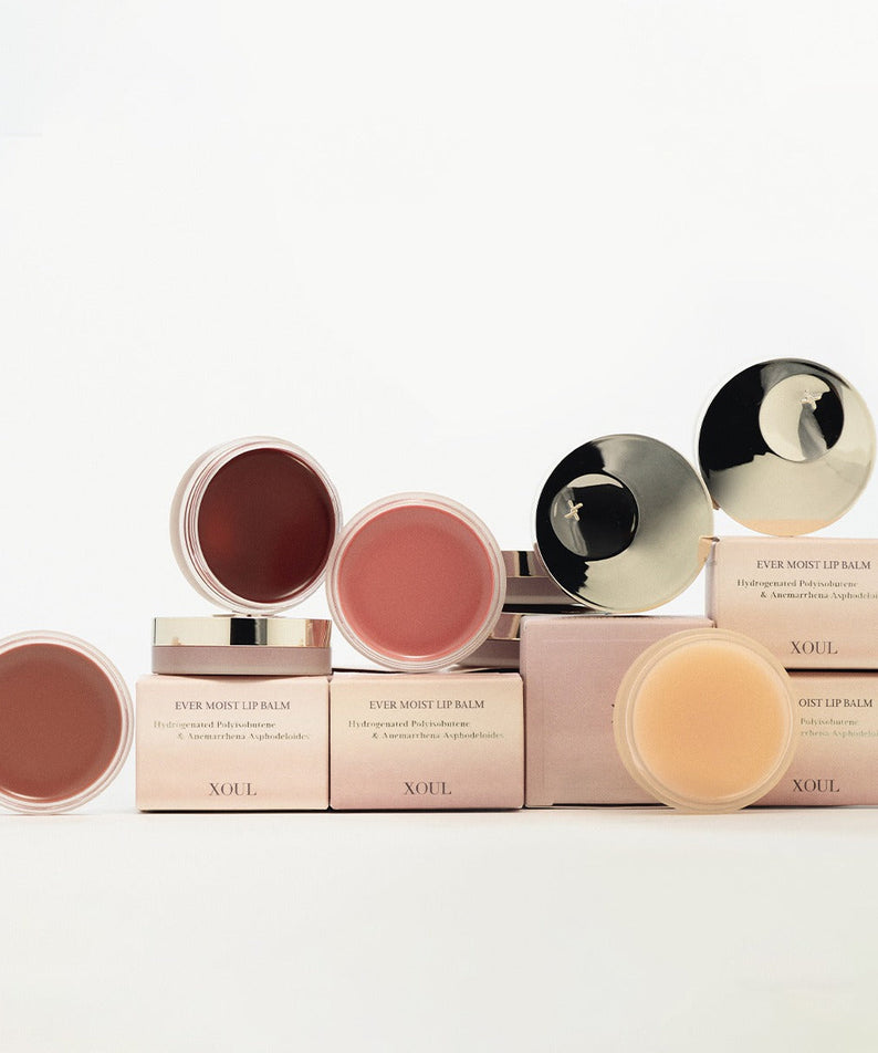 Décris l'image en français : XOUL Ever Moist Volume Lip Balm 8g de la marque XOUL, baumes sur fond blanc, étuis et couvercles dorés.