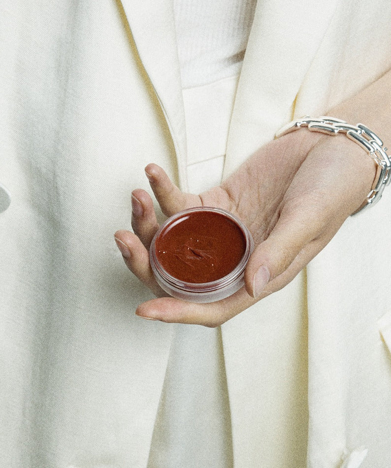 Décris l'image en français : XOUL Ever Moist Volume Lip Balm 8g de la marque XOUL, baume brun dans la main.
