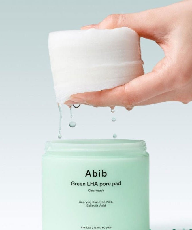 ABIB Green LHA Pore Pad Clear Touch 60 Sheets sur fond vert, main tenant tampon imbibé pour soin de la peau.