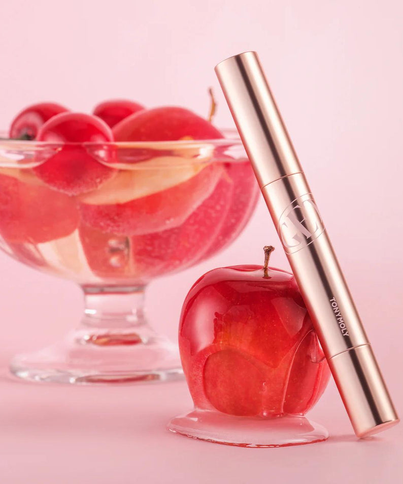 TONY MOLY Get It Tint Glaze Balm, tube doré sur fond rose, baies rouges en arrière-plan—produit de maquillage.