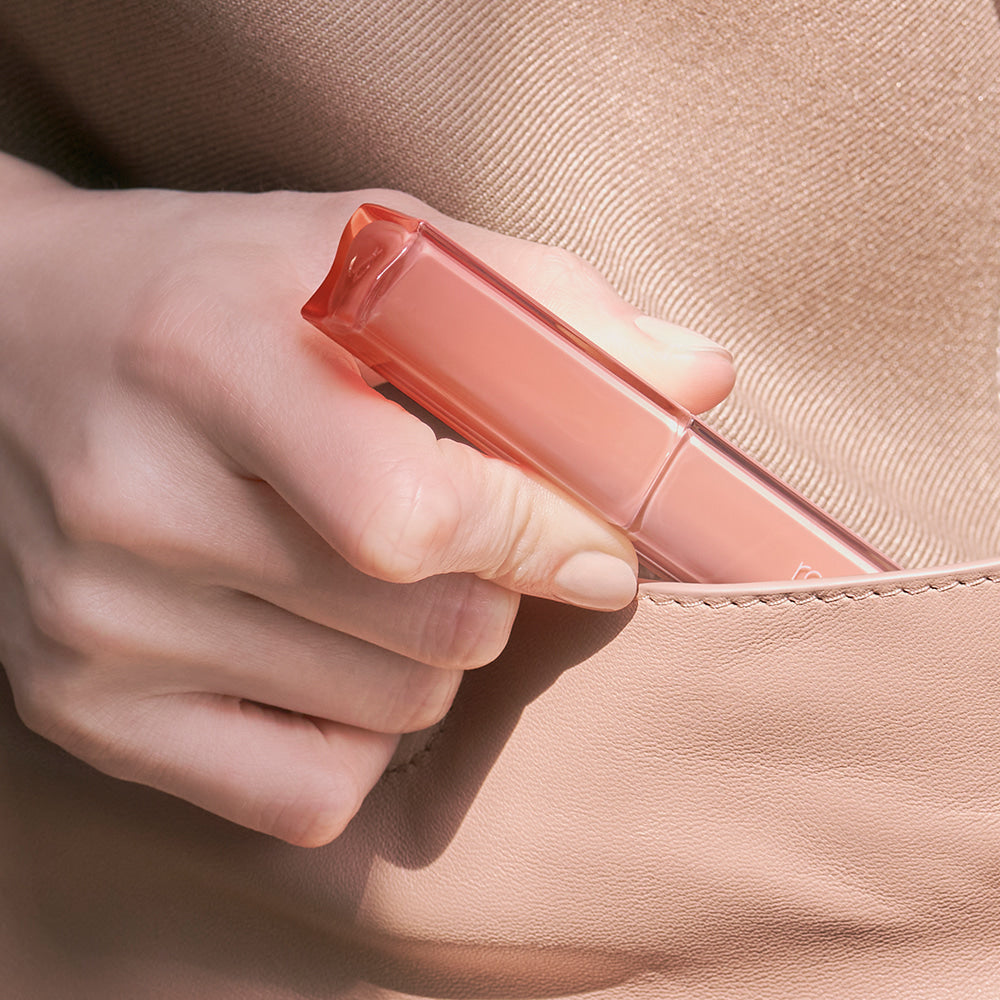 ROMAND Sheer Tinted Stick de la marque ROMAND, main tenant le stick teinté sur peau, fond cuir beige.