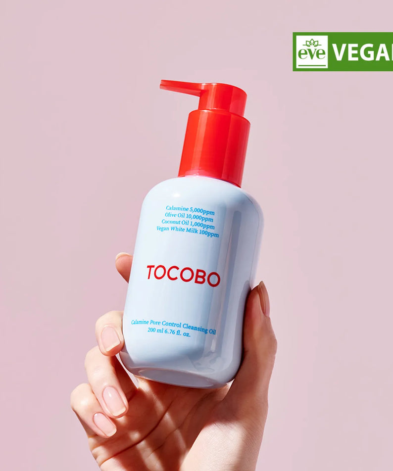 Main tenant TOCOBO Calamine Pore Control Cleansing Oil 200ml, flacon bleu à pompe rouge sur fond rose, vegan