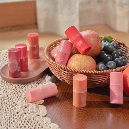 ROMAND Bare Water Tint de la marque ROMAND, maquillages rouges en décor nature avec fruits et paniers, sur tissu beige.