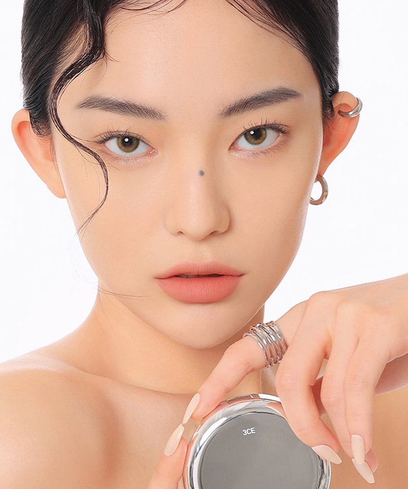 Décris l'image en français avec 3CE  Makeup Fix Powder 9g : poudre fixatrice 3CE sur une femme maquillée, fond blanc, gros plan.